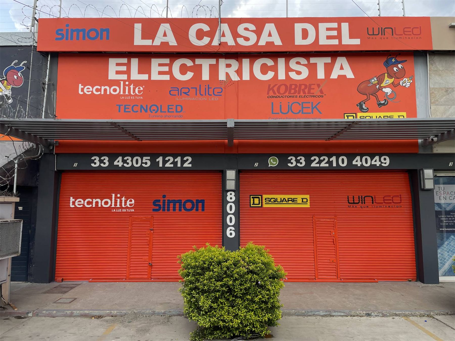 Fachada naranja de La Casa del Electricista con marcas y teléfonos.