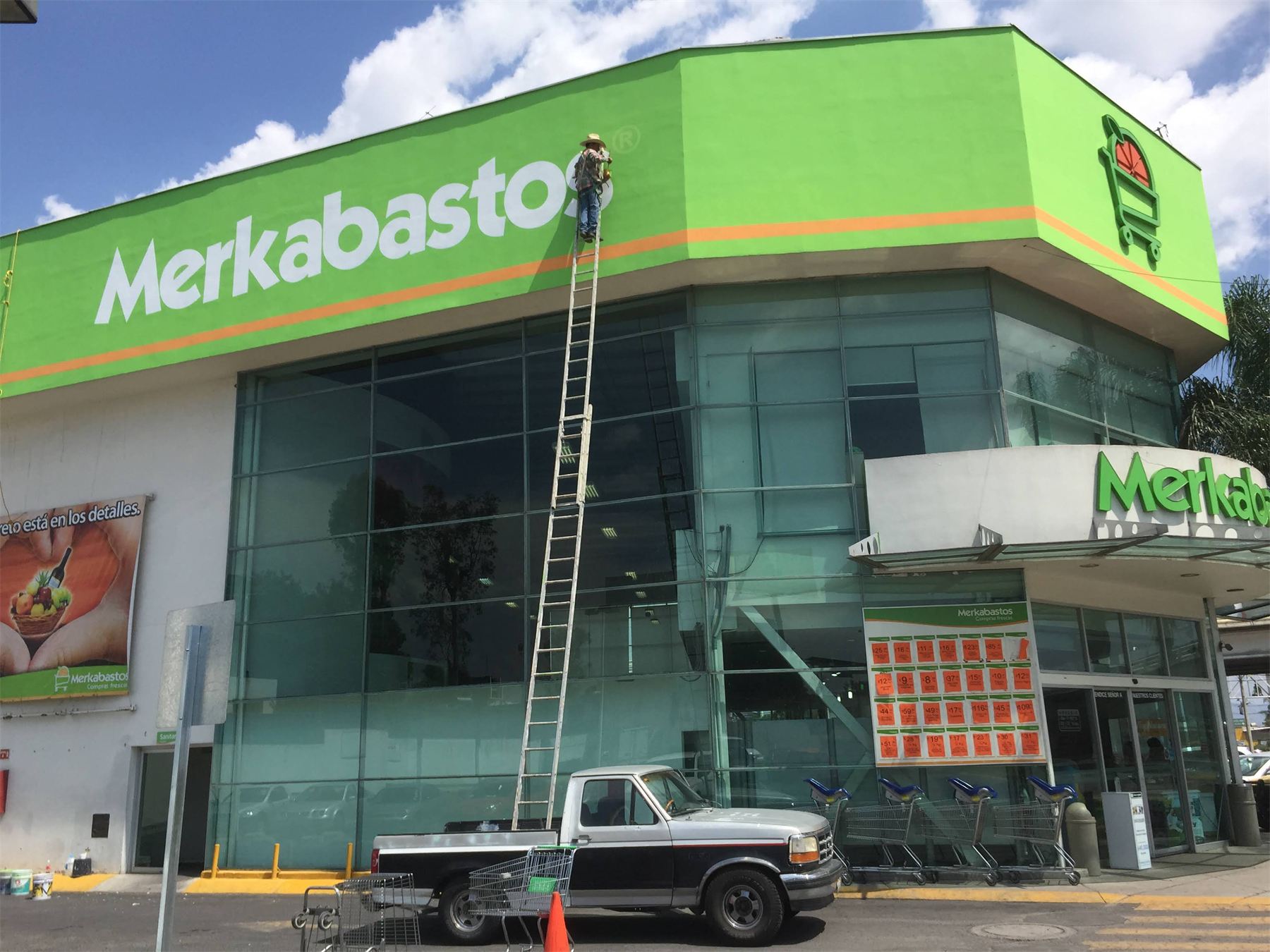 Instalación de la identidad de Merkabasto en fachada verde de dos niveles.