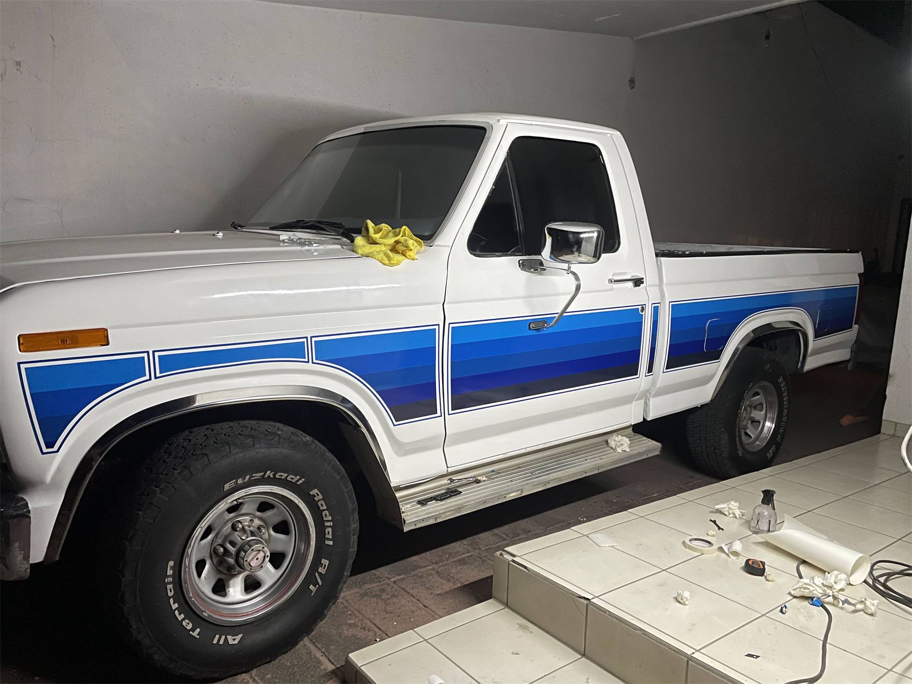 Camioneta Ford clásica blanca con franjas azules aplicadas en el costado.