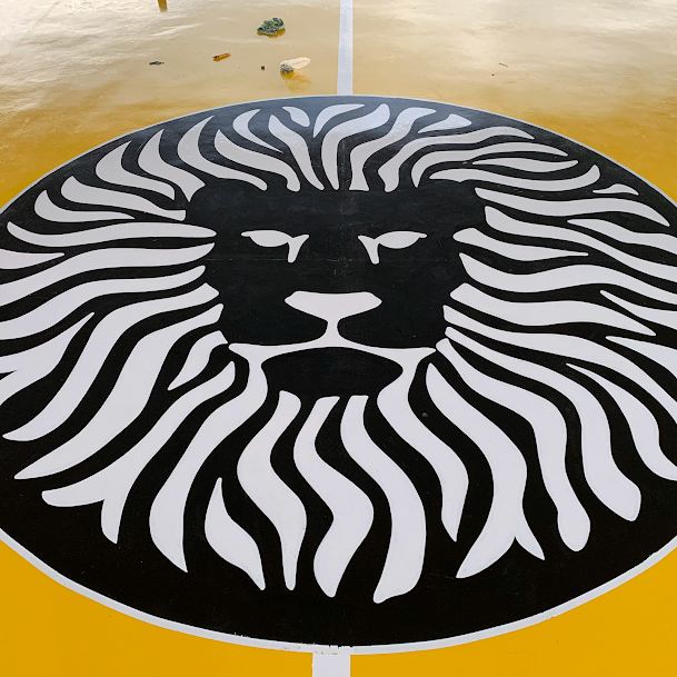 Cabeza de león pintada en blanco y negro sobre piso deportivo amarillo.